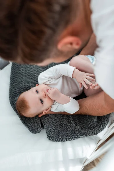 Blick von oben auf einen Mann, der sich über einen entzückenden kleinen Sohn beugt, der in einem Babybett auf einer Decke liegt — Stockfoto