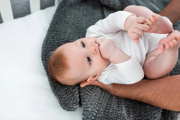 Обрізаний вид людини, що торкається чарівного немовляти, що лежить у дитячому ліжечку на ковдрі, вибірковий фокус — стокове фото