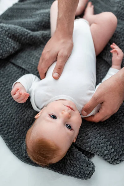 Abgeschnittene Ansicht eines Mannes, der einen entzückenden kleinen Jungen berührt, der auf einer Decke liegt — Stockfoto