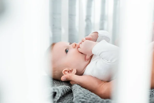 Cropped view of man touching cute infant lying in baby cot, selective focus — Stock Photo