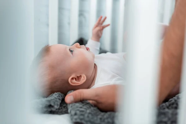 Cropped view of man touching adorable son lying in baby cot, selective focus — Stock Photo