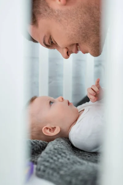 Enfoque selectivo de hombre sonriente apoyado por encima de bebé lindo acostado en cuna - foto de stock