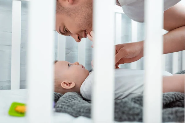 Selective focus of happy young father touching cute baby boy lying in baby cot — Stock Photo