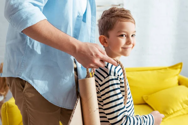 Cropped view of man fixing carton plane wings on back of happy son — Stock Photo