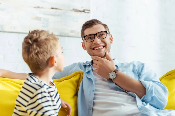 Selektiver Fokus eines lächelnden Mannes, der sein Kinn berührt, während er mit seinem entzückenden Sohn spricht — Stockfoto