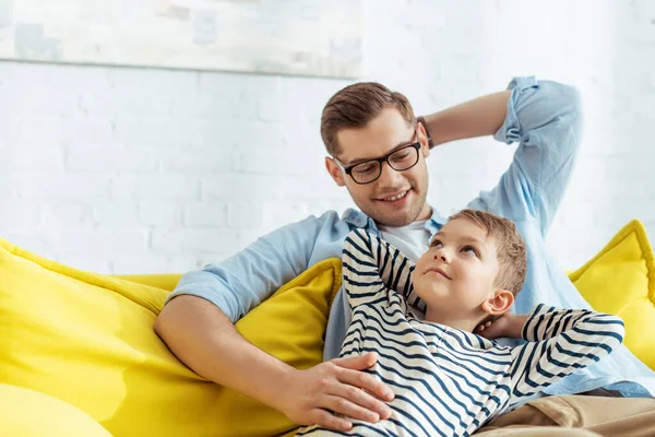 Щасливий батько і деякі дивляться один на одного, сидячи на дивані вдома — стокове фото