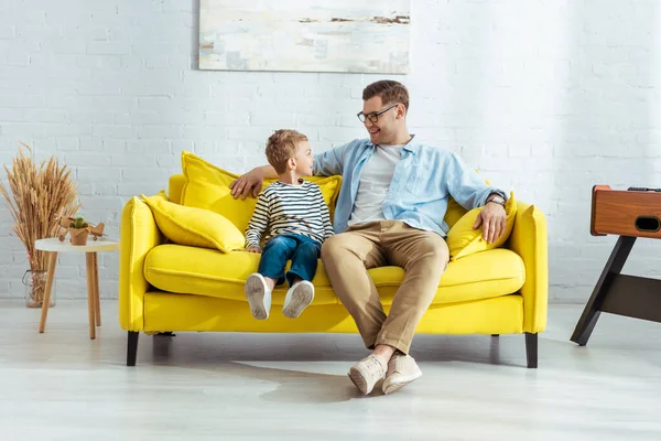 Heureux père et fils parler tout en étant assis sur le canapé jaune — Photo de stock