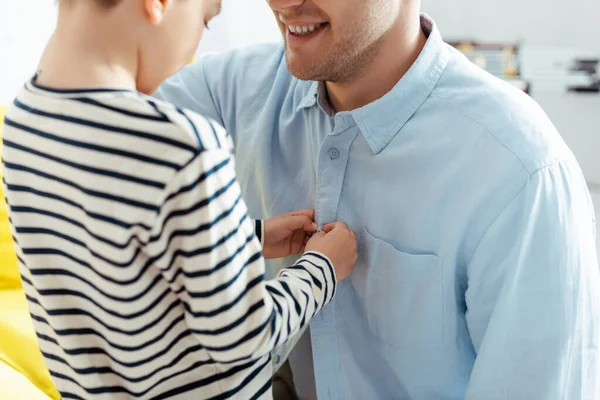 Cropped view of boy buttoning shirt of smiling father — Stock Photo