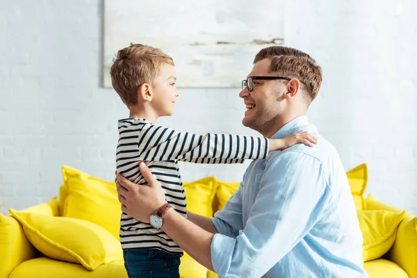 Seitenansicht eines lächelnden Jungen, der die Hände auf den Schultern seines glücklichen Vaters hält — Stockfoto