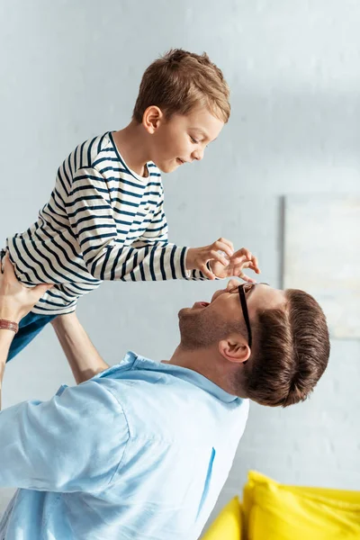 Adorable boy showing scaring gesture to father holding him on hands over head — Stock Photo