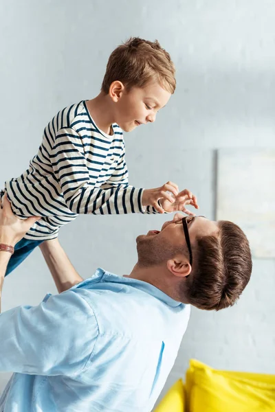 Adorable garçon montrant geste effrayant au père le tenant sur les mains au-dessus de la tête — Photo de stock