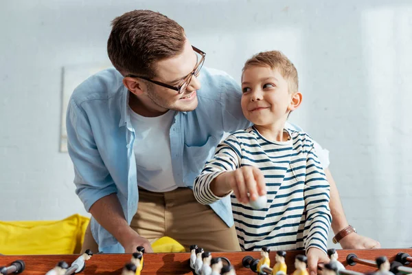 Feliz padre e hijo mirándose mientras juegan al futbolín - foto de stock