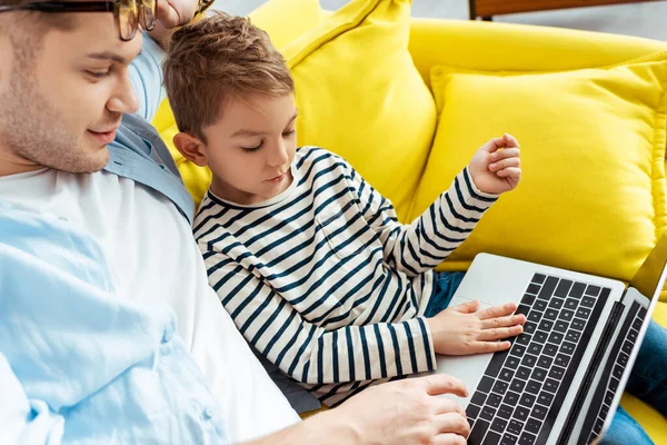 Vue grand angle du père et du fils en utilisant un ordinateur portable ensemble — Photo de stock