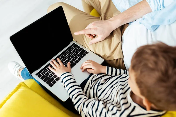 Ausgeschnittene Ansicht des Vaters, der mit dem Finger zeigt, während Sohn Laptop mit leerem Bildschirm benutzt — Stockfoto