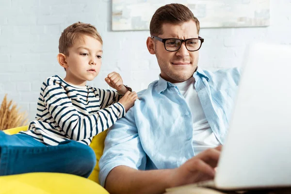 Cute child sitting near attentive father using laptop — Stock Photo