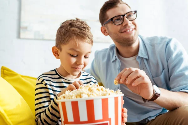 Selective focus of concentrated, excited man watching tv while eating popcorn with son — Stock Photo