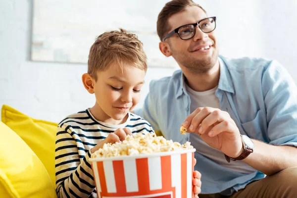 Enfoque selectivo de concentrado, hombre emocionado viendo la televisión mientras come palomitas de maíz con su hijo - foto de stock