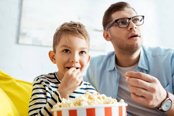 Attentive father and son watching tv and eating popcorn at home — Stock Photo