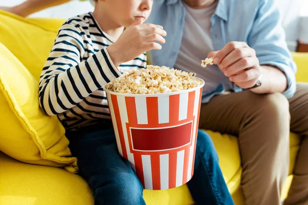 Cropped view of father and son eating popcorn from paper bucket — Stock Photo