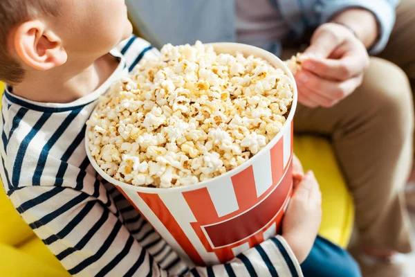 Vista recortada de niño sosteniendo cubo de palomitas de maíz cerca de padre - foto de stock