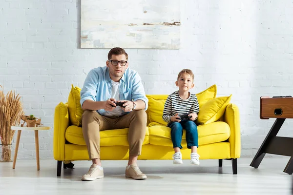 KYIV, UCRANIA - 9 de junio de 2020: padre e hijo concentrados jugando videojuegos con joysticks - foto de stock