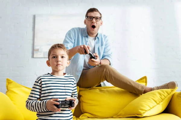 KYIV, UCRANIA - 9 de junio de 2020: niño atento y padre emocionado jugando videojuegos con joysticks - foto de stock