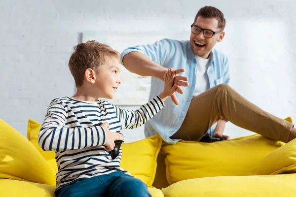 KYIV, UKRAINE - JUNE 9, 2020: cute boy holding joystick and giving high five to smiling father — Stock Photo