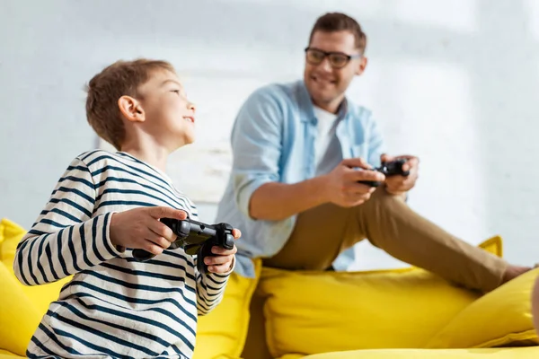 KYIV, UKRAINE - JUNE 9, 2020: selective focus of happy boy and smiling father playing video game with joysticks — Stock Photo