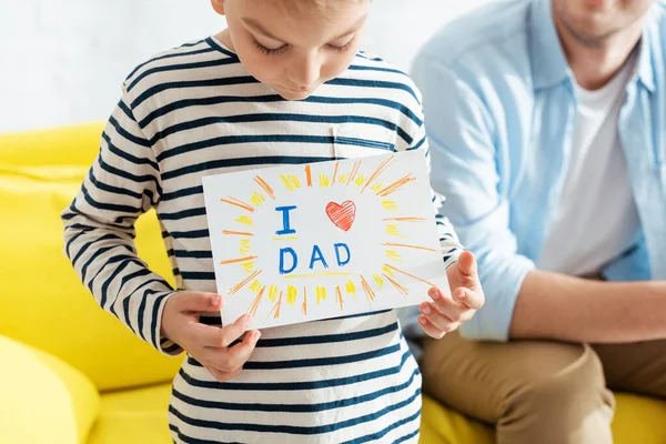 Vue recadrée de l'homme près du fils montrant la carte de voeux de jour des pères avec lettrage et symbole de coeur — Photo de stock