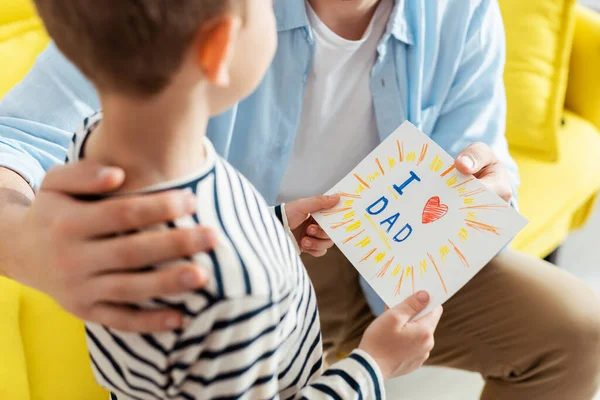 Ausgeschnittene Ansicht von Vater umarmt Sohn überreicht ihm handgemachte Grußkarte zum Vatertag mit Schriftzug und Herzsymbol — Stockfoto