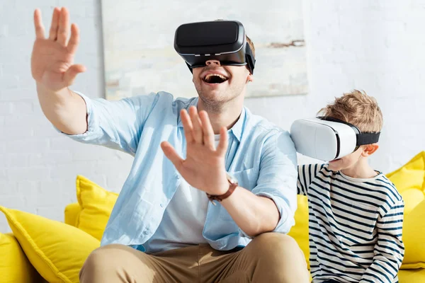 Возбужденный мужчина жестикулирует с протянутыми руками, используя VR-наушники вместе с сыном — стоковое фото