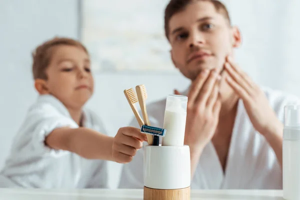 Foyer sélectif de l'homme touchant le visage tout en adorable fils prenant brosse à dents — Photo de stock