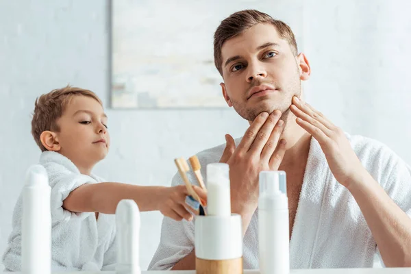 Jeune père touchant visage tandis que adorable fils prenant brosse à dents — Photo de stock