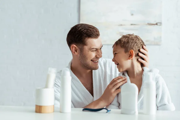 Enfoque selectivo de padre feliz tocar hijo cerca de artículos de tocador en el baño - foto de stock