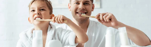 Selective focus of happy father and son brushing teeth together, panoramic shot — Stock Photo