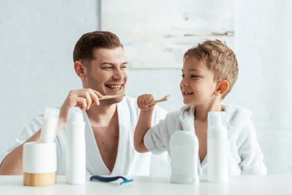 Foco seletivo de pai e filho felizes olhando um para o outro enquanto escovando os dentes juntos — Fotografia de Stock