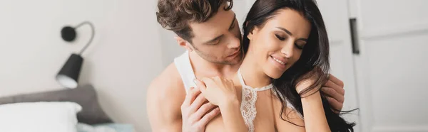 Cosecha panorámica del hombre guapo abrazando a la mujer sonriente en el sujetador en el dormitorio — Stock Photo