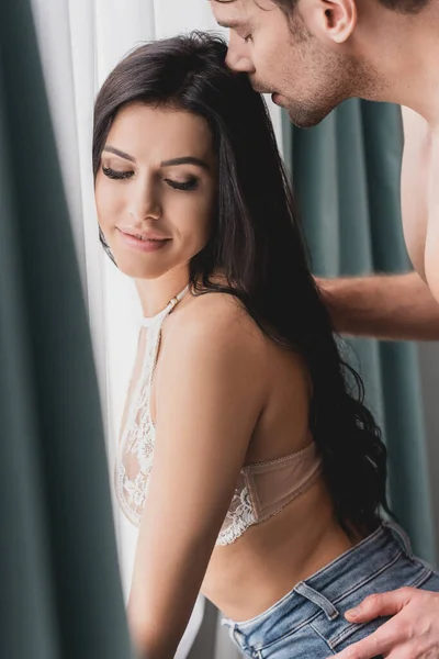 Side view of shirtless man embracing sensual smiling woman near window — Stock Photo