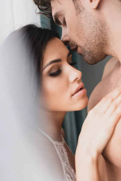 Selective focus of beautiful woman touching muscular boyfriend near window at home — Stock Photo