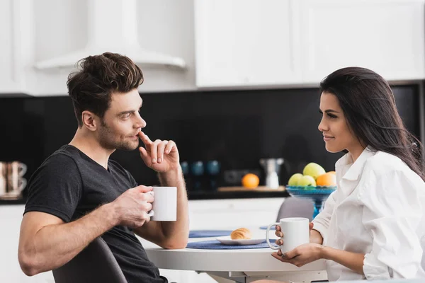 Красива жінка тримає чашку кави і дивиться на гарного хлопця на кухні — стокове фото