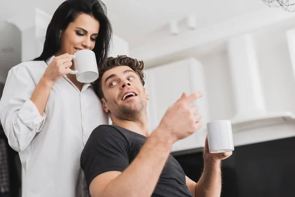 Selektiver Fokus eines gutaussehenden Mannes mit einer Tasse Kaffee in der Nähe einer lächelnden Freundin im Hemd — Stockfoto