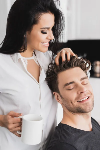 Smiling woman in shirt holding cup of coffee and touching hair of handsome boyfriend — Stock Photo