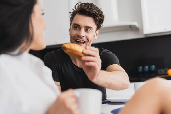 Selektiver Fokus des positiven Mannes, der mit einer Tasse Kaffee Croissant in der Nähe seiner Freundin hält — Stockfoto