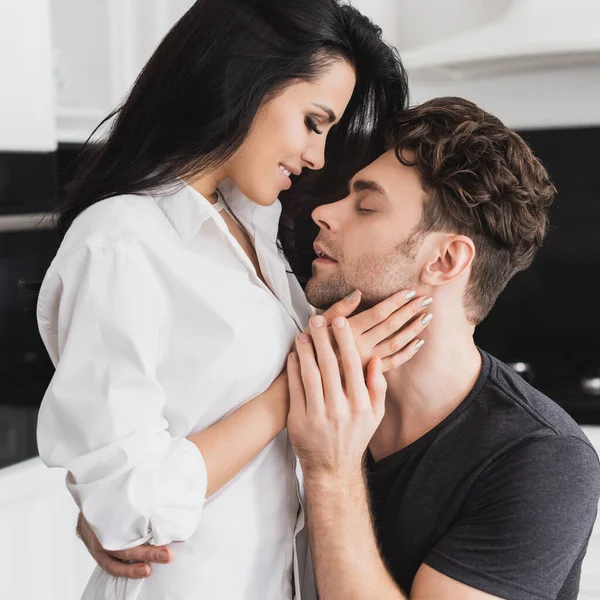 Mujer sonriente en camisa tocando el cuello de novio guapo en casa - foto de stock