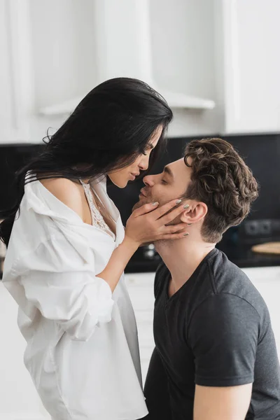 Side view of sexy woman in shirt kissing handsome boyfriend at home — Stock Photo