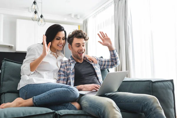 Pareja sonriente que tiene videollamada en el portátil en la sala de estar - foto de stock