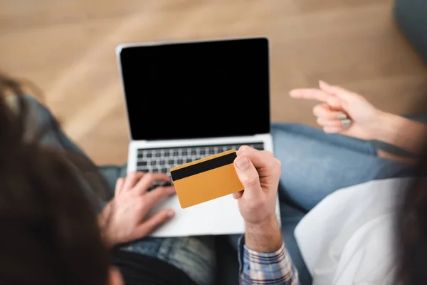 Overhead view of man holding credit card while girlfriend pointing with finger at laptop — Stock Photo