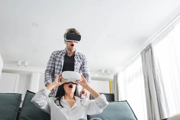 Casal chocado usando fones de ouvido realidade virtual na sala de estar — Fotografia de Stock