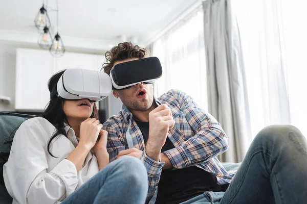 Selective focus of scared young couple using vr headsets on couch — Stock Photo