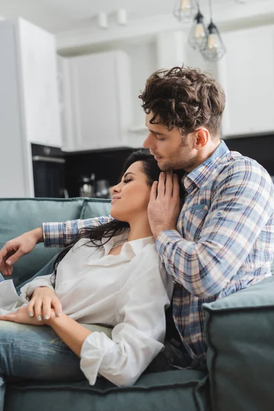 Selective focus of handsome man touching hair of attractive girlfriend on sofa — Stock Photo